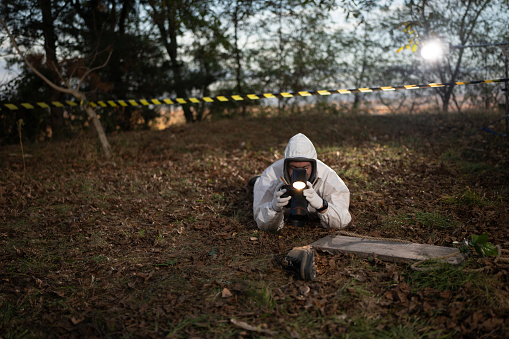 Male forensic scientist photographing evidence shoes with a camera at crime scene in the woods.