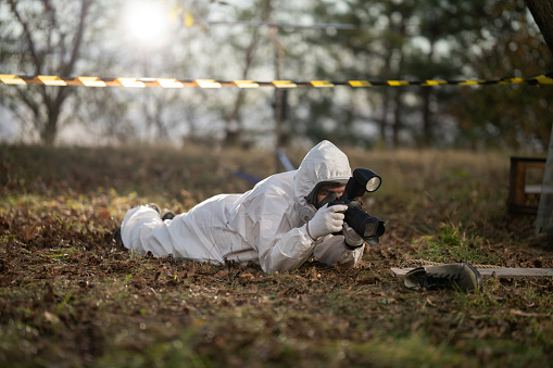Male forensic scientist photographing evidence shoes with a camera at crime scene in the woods.
