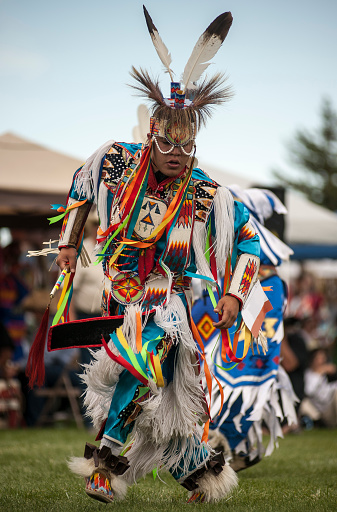 A young Native American man moves quickly to the rhythm of drums at a PowWow dance competition.