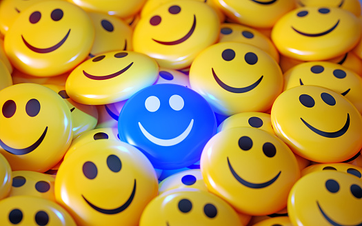 Blue happy face emoji surrounded by yellow happy face emojis. Horizontal composition.