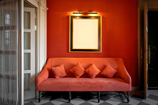 Mockup with a frame for a picture or photo on a red wall above a sofa in a classic interior.