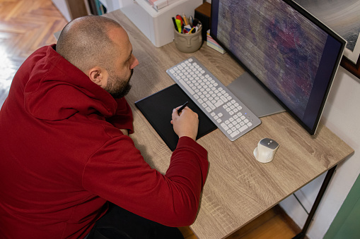 Photo series of a digital artist working at his home studio/office while drawing a digital painting on a digital surface/tablet.