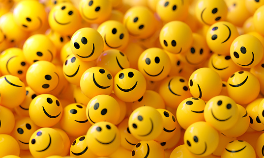 Yellow spheres textured with happy face emoji on yellow background. Horizontal composition.