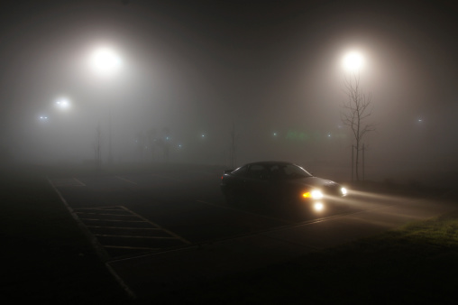 A car in a parking lot on a foggy night.