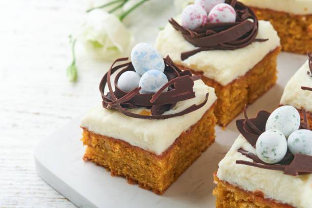 istock Easter carrot cake bars decorated with chocolate nest and chocolate candy eggs blossoming cherry or apple flowers on rustic light wooden backgrounds. Easter holiday meal. Traditional Easter food. 1872242434