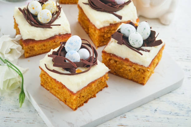 istock Easter carrot cake bars decorated with chocolate nest and chocolate candy eggs blossoming cherry or apple flowers on rustic light wooden backgrounds. Easter holiday meal. Traditional Easter food. 1872243505
