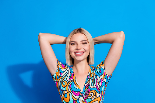 Portrait of toothy beaming positive girl wear stylish shirt keep hands behind head relaxing isolated on vivid blue color background.