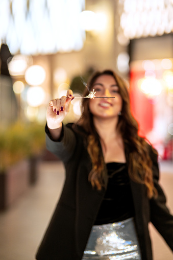 Beautiful woman holding sparkle in hand as she celebrates New Year in the city