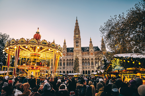 Illuminated carousel on town square full of people in front of Vienna Town Hall at time of the Christmas market named Wiener Christkindlmarkt