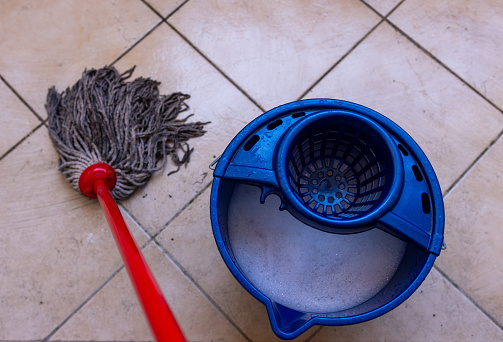 Dirty mop on tiles with a bucket of soapy water