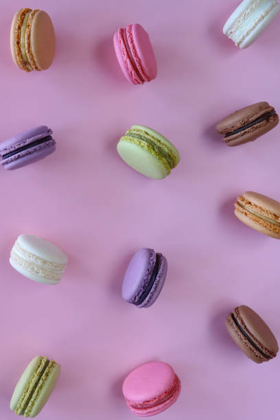 istock Full frame image of group of multi coloured macarons filled with flavoured butter cream standing on edge, strawberry, vanilla, blueberry, orange, pistachio, chocolate flavoured meringues, purple background, elevated view 1872258621
