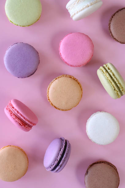 istock Full frame image of group of multi coloured macarons filled with flavoured butter cream some standing on edge, strawberry, vanilla, blueberry, orange, pistachio, chocolate flavoured meringues on pink background, elevated view 1872258629