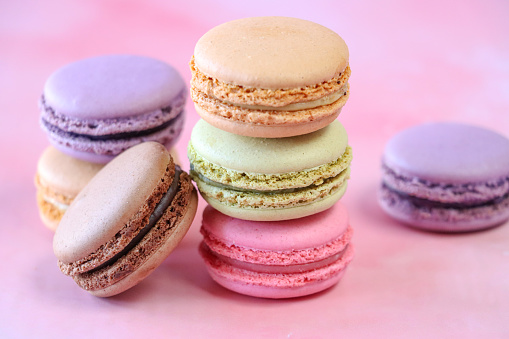 Stock photo showing close-up view of a stack of multi coloured macarons on a purple background. Pink strawberry, brown chocolate, purple blueberry, green pistachio and orange flavoured meringues.