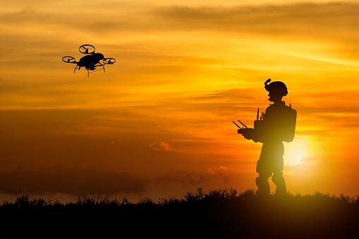 An army soldier's silhouette operating a tactical drone against the backdrop of a setting sun, depicting a military operation.