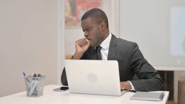 istock Coughing African Businessman Using Laptop while Sitting in Office 1872297450