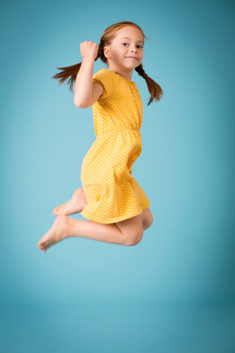 Color image of a red-haired, seven year old girl, leaping up in the air, with blue background.