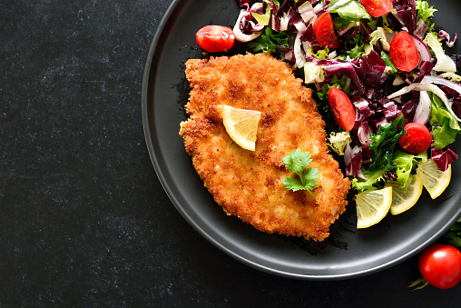 Chicken schnitzel and vegetable salad on plate over dark background with copy space. Top view, flat lay