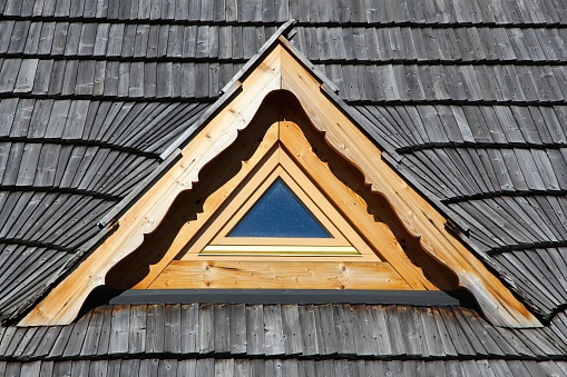 Triangular attic window in a house covered with wooden shingle roof. Folk architecture design in Podhale region in Poland.
