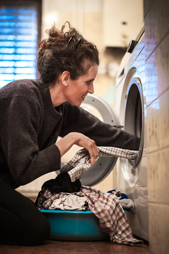 Adult Woman Putting Laundry in the Washing Machine in Domestic Bathroom