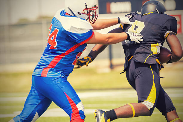 jogador de futebol americano correndo para aterrissagem enquanto tenta resolver adversário - football player group of people running american football - fotografias e filmes do acervo