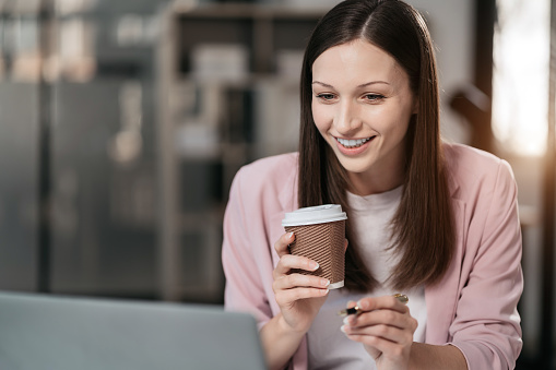 portrait of a business woman Self-confident young woman sit holding coffee mug and working laptop.  Casual business. Self-confidence.