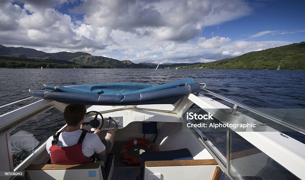 Rented motor boat on Coniston Water Young man and younger boy driving a rented motor boat on Coniston Water in the English Lake District. Adult Stock Photo