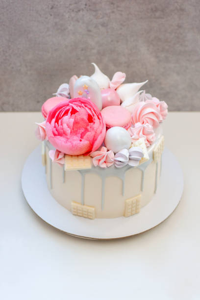 istock Beautiful and elegant cake decorated with melted grey chocolate, macaroons, edible pink peony flower, chocolate bites and meringues 1872373833