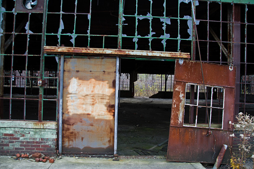 Derelict industrial warehouse with rusty metal door, broken windows, and decaying infrastructure in Indiana, Warsaw. Capturing the eerie atmosphere of urban decay and forgotten history.