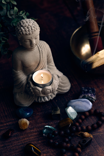 stone statue of buddha with a candle and gems on dark background