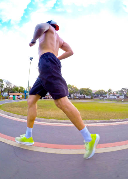 Young man running on an asphalt track in a wooded environment. Lateral left view