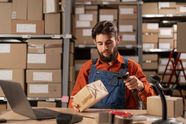 istock Young man working in factory warehouse scanning labels on the boxes with barcode scanner. 1872386483
