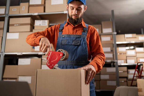 istock Young handsome man worker packing online orders using tape at storehouse 1872386485