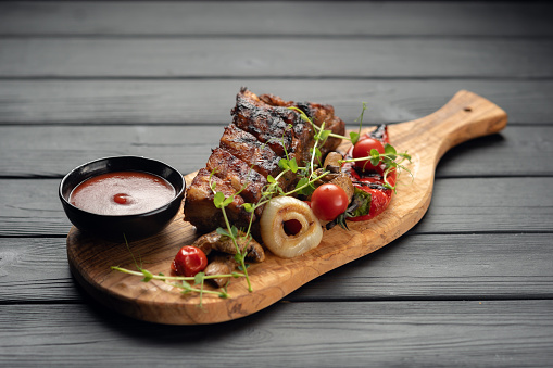 hot grilled spare ribs from a summer BBQ served with a grilled vegetables and sauce on an old vintage wooden cutting board. Copy space