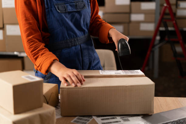 istock Close-up of female hands scanning barcode on delivery parcel box with scanner. Worker scan barcode before delivery at storage. 1872391228