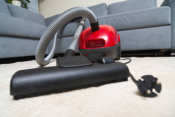 istock Red vacuum cleaner on carpeted floor beside gray sofa 187240605
