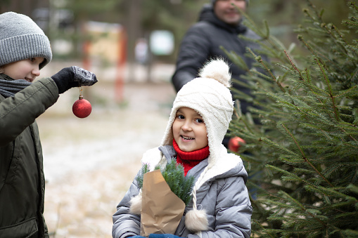 Cute little girl and boy with dad decorate a Christmas tree outside.