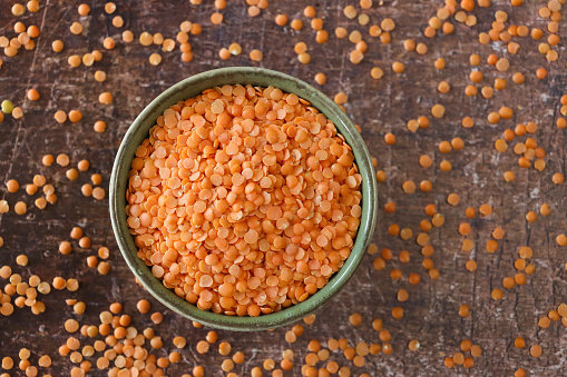 Stock photo showing close-up, elevated view of split red lentils that are piled high in a green, china bowl against a distressed brown background. Lentils are considered to be a very healthy food, containing a rich source of wealth of carbohydrates and proteins, as well as B vitamins, calcium, iron and phosphorus.
