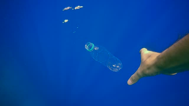 Plastic bottle slowly sinks into blue abyss, from bottle come out last air bubble