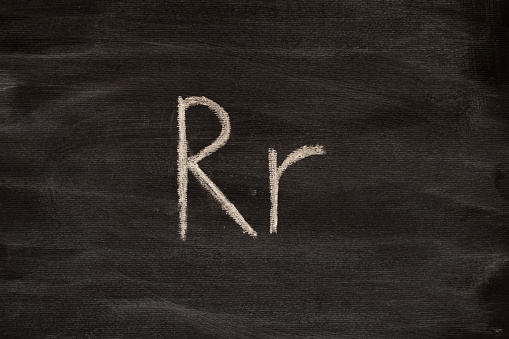 Английская буква R написанная мелом на черной доске. Крупным планом.