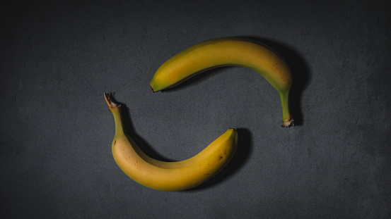 Two vibrant yellow bananas artfully arranged against a dark background, creating a visually striking contrast.