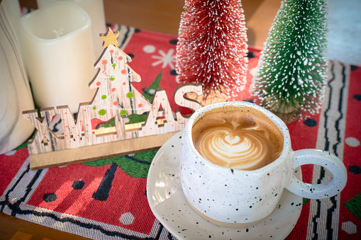 Close up of Hot coffee latte with latte art milk foam in cup mug with Xmas decors and Xmas tree baubles on wood desk Celebrating Merry Christmas and New year.