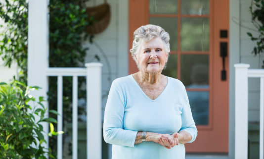 Portrait of elderly woman (90s) standing outside home.