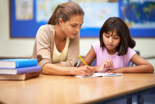 Shot of a teacher working with a young students while sitting in a classroom