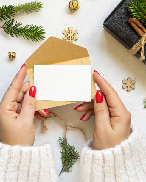 istock Hands with card and envelope near gift boxes, fir branches and Christmas decor, Mockup 1872456869