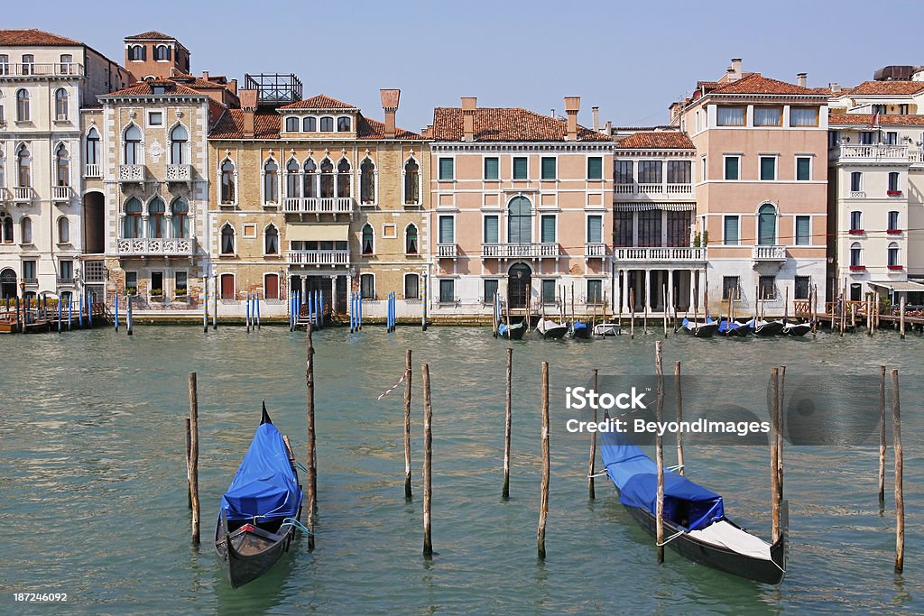 Moored gondolas on Venice canal In the foreground, two gondolas moored on vertical poles on Venice’s Grand Canal.  In the background is a row of Venetian buildings with a range of gondolas and other watercraft tied to poles.  Horizontal, copy space. Architecture Stock Photo