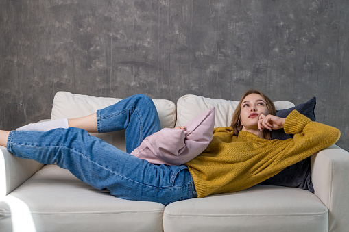 young woman is lying on the sofa with a pillow in her hand and dreamily looks up. daydreams on the couch