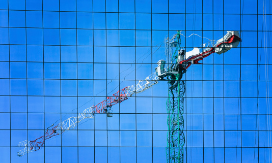 Reflection of a construction crane in windows of modern office building.