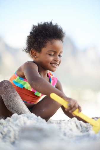 An adorable young girl building a sand castle at the beach