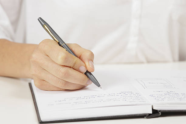 istock A hand writing in a book with a silver pen. 187248729