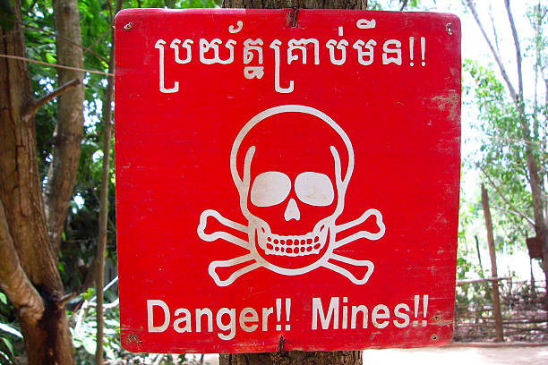 Red landmine warning sign in Cambodia Red landmine warning sign in Angkor, Cambodia.  Skull and crossbones with “Danger!!” and “Mines!!”. land mine stock pictures, royalty-free photos & images